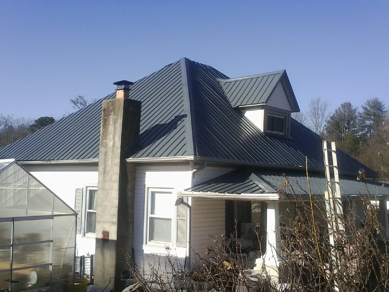 Dark blue standing seam metal roof on a white farmhouse with dormer — Slate & Tile Roof Repair by Roofing Brothers in Painter