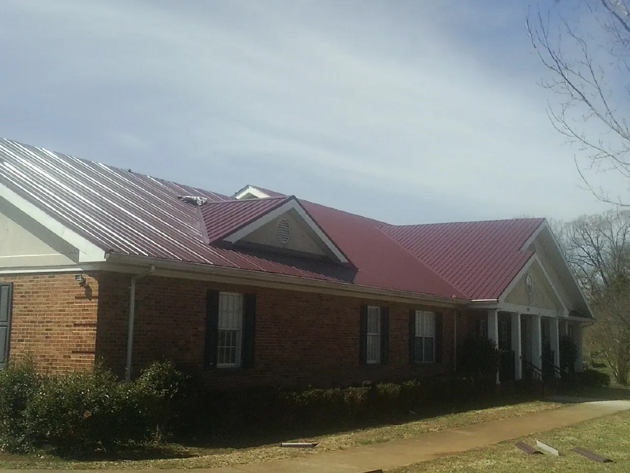 Red metal roof with gabled entries on a long brick building, from a Hail Damage Roof Repair job in Painter