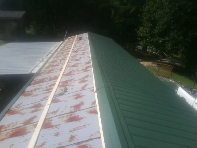 Old rusted panels beside newly installed green metal roofing — Wind Damage Roof Repair by Roofing Brothers in Painter