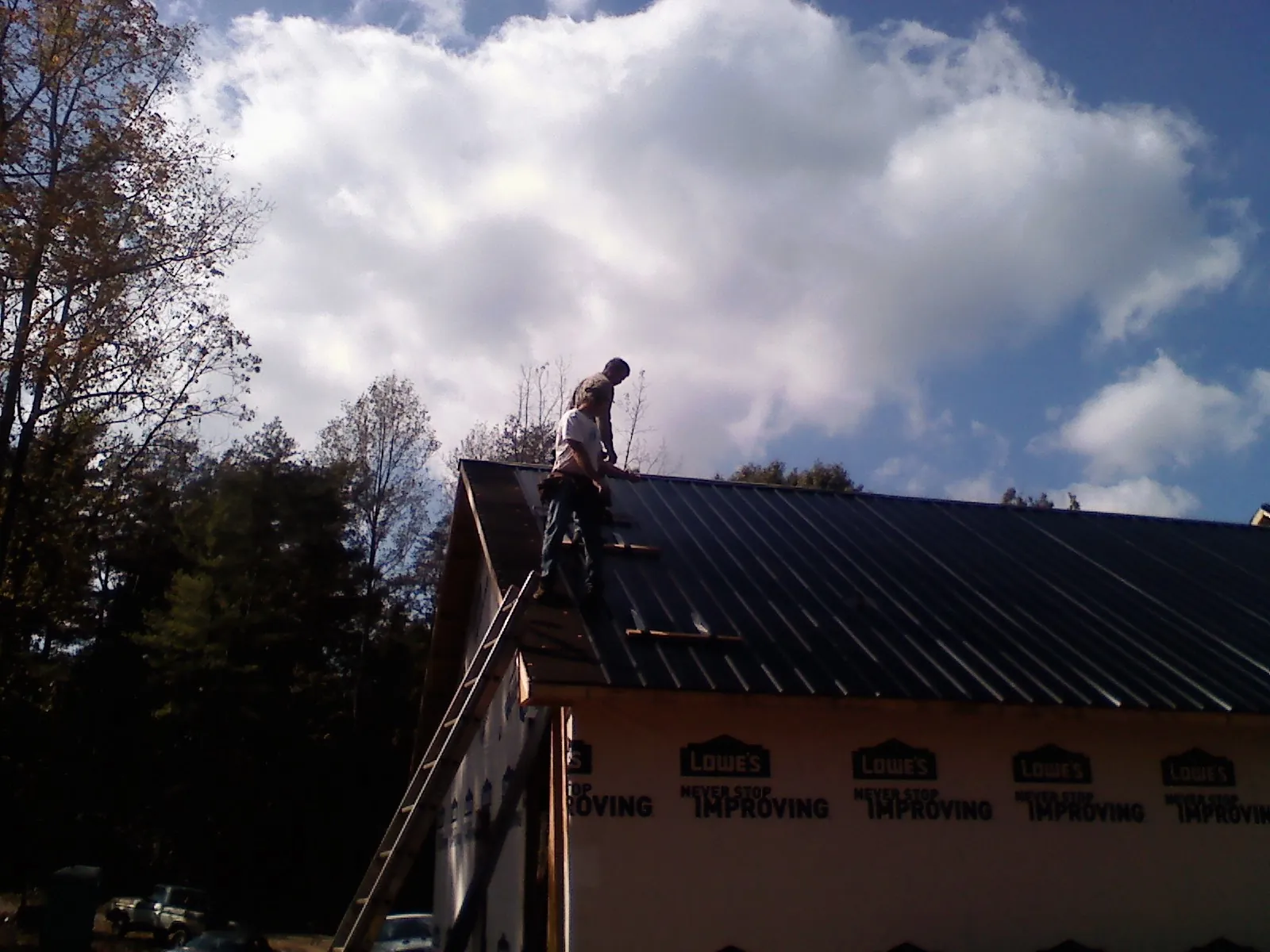 Roofer fastening dark metal panels high against a cloudy sky, from a Roof Inspection job in Painter