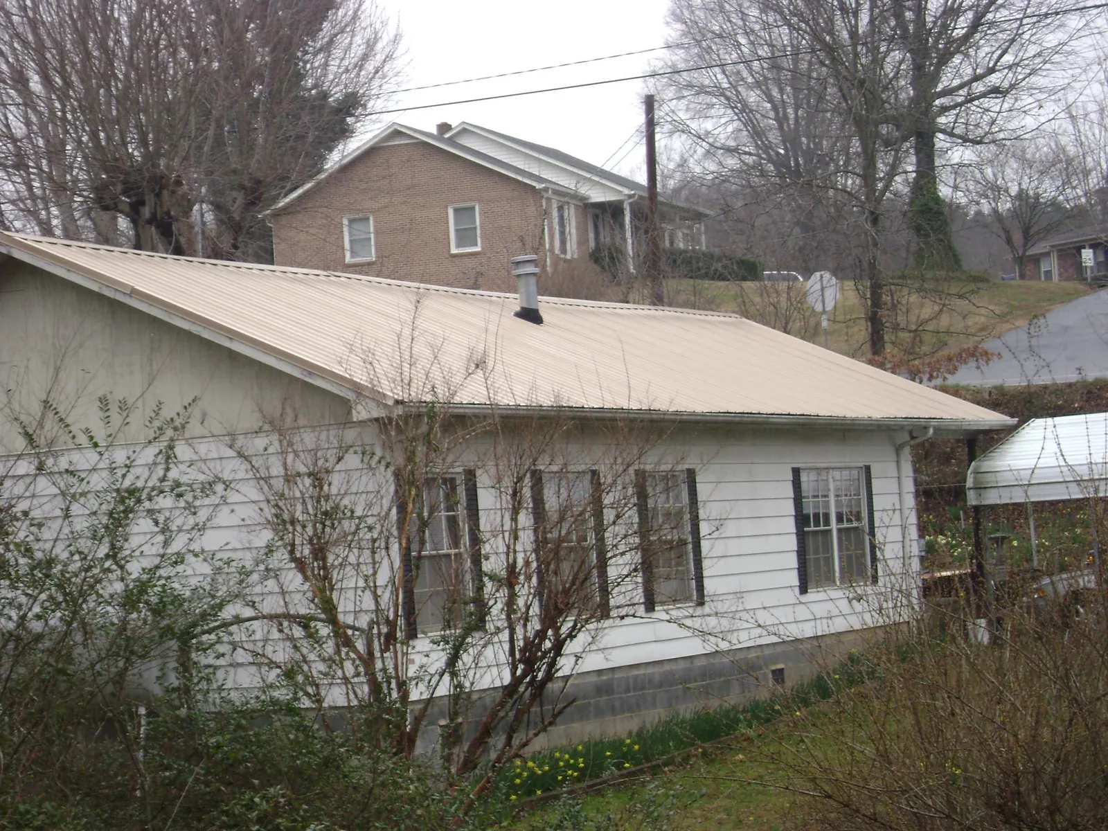 Tan metal roof on a white sided house set into a hillside — Commercial Roofing by Roofing Brothers in Painter