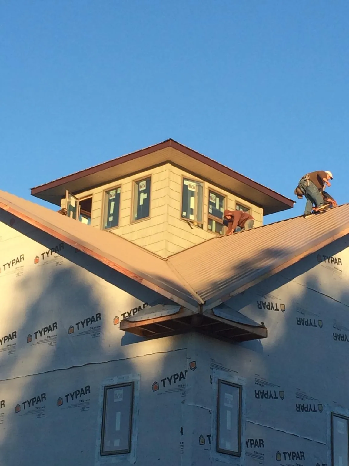 Roofers working around a rooftop cupola on a new metal roof at sunset in Painter